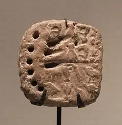 Petite tablette en forme de coussin avec une scène imprimée et des signes ronds et linéaires.