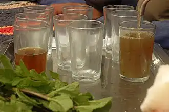 Un verre à moitié rempli, plusieurs verres vides, un verre en train d'être rempli de thé dans lequel se trouvent de nombreux résidus.