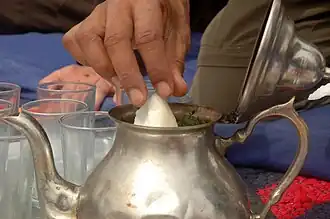 Une main plonge un pain de sucre dans la théière.