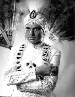 Photo tirée d'un film, un personnage de maharadjah avec un turban et un costume blanc.