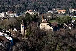 Une tour avec un toit pointu et une horloge bleue et un bâtiment en pierres avec des volets rouges et jaunes et une tour au toit pointu.
