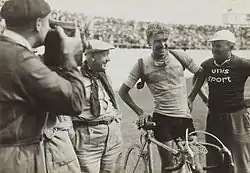 Photographie d'un cycliste souriant entouré par trois hommes après l'arrivée de la course.