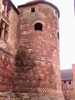 Vue générale d'une tour vue de la gauche, avec un bâtiment comportant deux fenêtres à meneaux à gauche et un bâtiment construit en colombages à l'arrière-plan