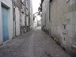 Photographie en couleurs d'une rue pavée, vue en enfilade entre deux deux rangées de façades.