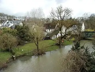 Photographie en couleurs de maisons en contrebas d'une route, au milieu d'arbres et au bord d'un cours d'eau.