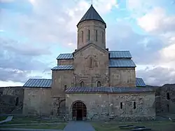 cathédrale de structure basilicale en pierres roses et grises à toits étagés surplombés d'un clocher décagonal.