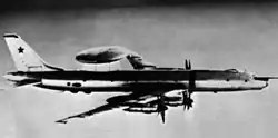 photo noir et blanc d'un avion-radar en vol. C'est un Tu-114 sur lequel a été montré un dome radar, en forme de soucoupe, au dessus de l'arrière du fuselage.