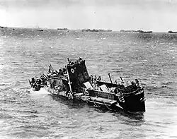 Photo noir et blanc d’un bateau de petite taille incliné, avec de nombreux autres navires en arrière-plan