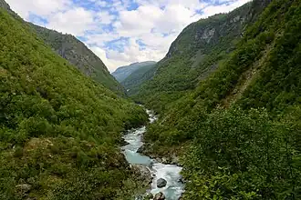 Vallée étroite et boisée avec un torrent en son sein.