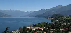 Panorama d'un lac de couleur bleu azur, bordé par les montagnes. On distingue une ville dans la forêt qui borde le lac.