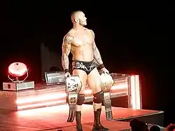 Randy Orton en slip entrant sur le ring avec une ceinture dans chaque main.