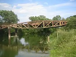 Le pont de Vacherauville date de 1944, il provient des travées du port Mulberry ayant servi au débarquement de 1944. C’est un pont historique, il n’en reste plus beaucoup en France, un morceau d’Histoire de la Seconde Guerre Mondiale là où la Première a fait des ravages. Ce pont a permis aux paysans vacherauvillois de rejoindre l’autre bord du canal de la Meuse. Ces deux travées ont été apportées ici, à Vacherauville, en 1960.