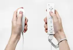 Une télécommande Wii et une manette Nunchuk, deux manettes de jeux vidéo de forme allongée en plastique blanc.