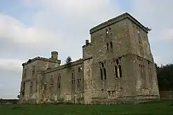 Photo en couleurs d'une grande demeure en ruines mais dont les murs sont encore debout, une tout carrée au premier plan