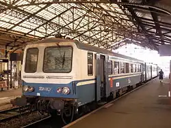 Autorail gris, bleu et blanc à quai sous la marquise d'une gare.