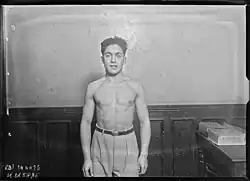 Photographie de presse en noir et blanc d'un homme musclé, torse nu, regardant l'objectif.