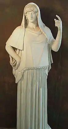 Statue d'Hestia en marbre. La déesse porte une robe longue et un voile sur la tête. Elle lève le bras gauche.
