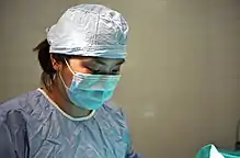 photographie : une femme en tenue de chirugienne penchée vers quelque chose