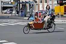 Photographie d’une femme sur un vélo disposant d’un coffre en bois à l’avant.