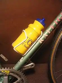 Photographie d’un cadre de vélo avec une tige métallique supportant une gourde en plastique jaune.