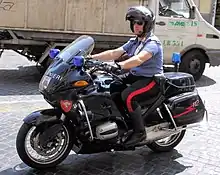 Photographie d'un homme en tenue bleue sur une moto floquée du mot carabinieri.