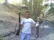 photographie : un homme dans un bois porte une carabine d'une main et un lapin mort de l’autre