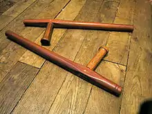 Photographie de deux tonfas posés sur un parquet.