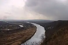 Photographie d'une rivière dans une méandre causée par un relief, avec des nuages gris dans le ciel.