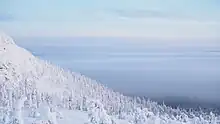 Photographie depuis une hauteur d'un versant de montagne totalement enneigée, avec en second plan de la brume qui dissimule le paysage.