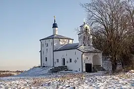 Photographe d'une église blanche orthodoxe avec un toit bleu, entourée d'un espace enneigé.
