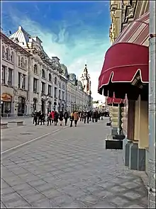 Vue actuelle de la rue bordée d'un bâtiment néo-classique en pierre gris pâle devant lequel passent des promeneurs