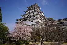 Château de pierre blanche de style oriental. Des cerisiers en fleurs sont également visibles.