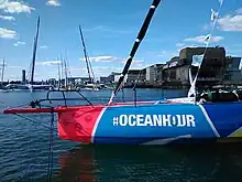 Gros plan de profil sur l'avant d'un voilier rouge, bleu et jaune, amarré à un ponton.