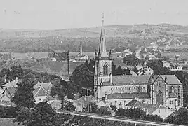 Photo noir et blanc montrant une église de style néogothique, groupes de maisons, terrils et divers bâtiments industriels.