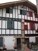 Vue d’une maison à pans de bois peint, en rouge pour la partie droite, en vert pour la partie gauche.