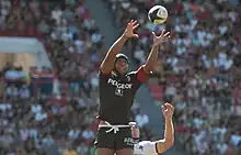 Joueur en l'air, tendant les deux bras en avant pour prendre un ballon en touche.