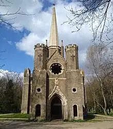 Chapelle en arrière plan entourée d'arbres et de feuilles mortes, image en couleur.