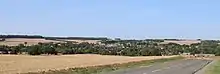 Panorama du village d'Agnicourt, au premier plan, niché au fond de la vallée de la Serre, avec le clocher de l'église qui émerge en bas à droite. Au loin, le clocher de l'église de Tavaux.