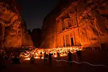 Vue nocturne d'un monument sculpté dans la roche. L'éclairage est assuré par un parterre de bougies. Des personnes observent le spectacle.