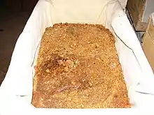 Plan rapproché d'une caisse en bois garnie de tissu blanc et remplie de résine en morceaux de tailles variées de couleur jaune clair à brun foncé.