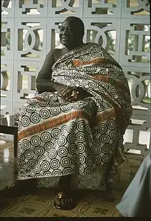 Un homme africain en vêtement traditionnel kente, assis avec des bagues en or.