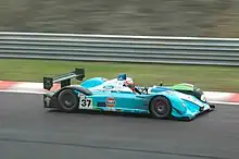 Photographie d'une voiture de sport-prototype bleu clair, noire et verte, vue de haut et de profil, sur une piste.