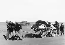 Photo en noir et blanc d'un petit groupe de personnes tirant une charrette.