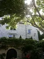 Photogtraphie en couleurs d'un b^^atiment pourvu d'une tourelle partiellement masqué par la végétation d'une cour.