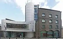 Un bâtiment en briques rouges, avec une extension moderne sur sa gauche, de couleur blanche.