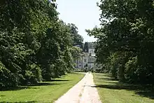 vue d'une allée bordée de chênes avec un le château des Genêts au fond