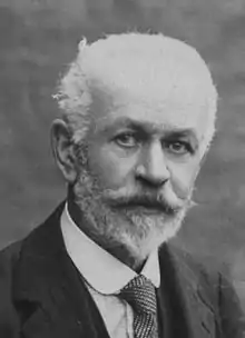 Photo noir et blanc d'un homme âgé, au crane partiellement dégarni et aux cheveux et barbe blanc.