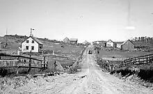 Un chemin de terre et des maisons de colons.