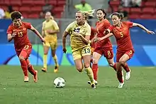 Photographie de la joueuse suédoise Fridolina Rolfö en train de courir avec le ballon suivie par trois joueuses chinoises.