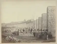 Photographie en sépia prise en contrebas du viaduc montrant des ouvrier du chantier, des piles sans arches et des arches en train d'être construites.